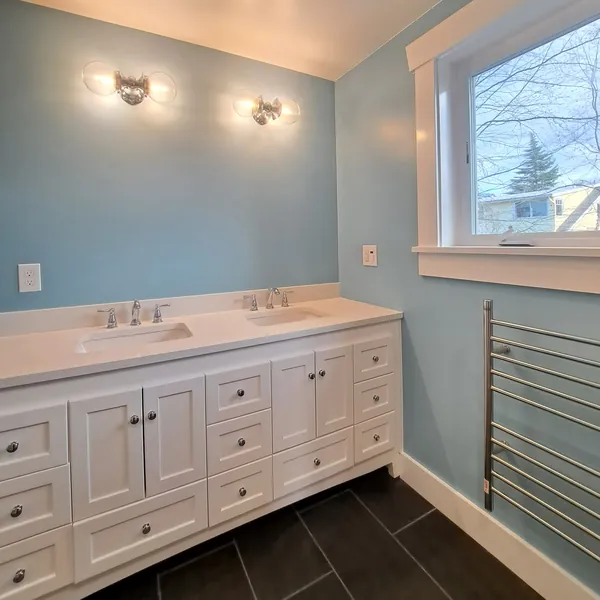 Bathroom with a white double vanity, quartz top, globe sconces, light-blue walls, dark tile floor and a heated towel rail