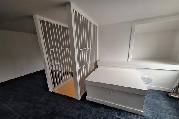 Finished attic bedroom with navy carpet, the slat partition at the stair and the built-in bench