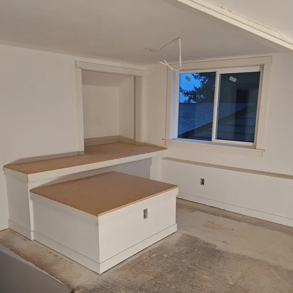 Attic bedroom under construction with bare subfloor and an unfinished built-in bench