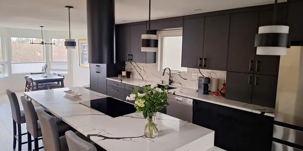 Kitchen with black flat-panel cabinets, a round black range hood and a marble-look quartz island with bar seating